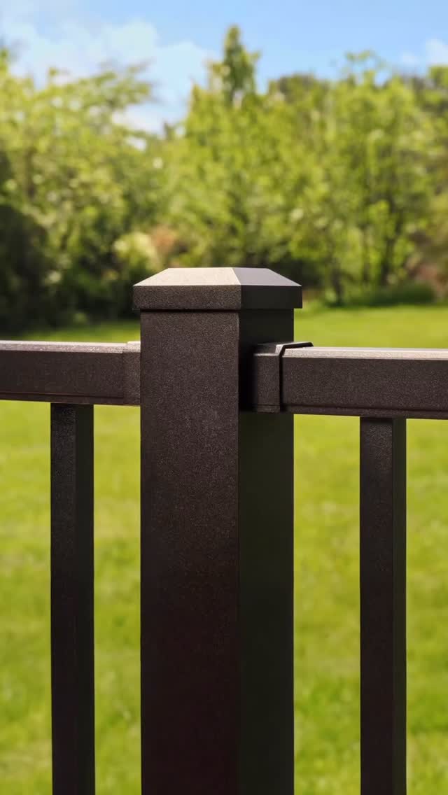 Close-up of a black metal deck railing post and guard on a Concepts Construction deck, with a green lawn behind it