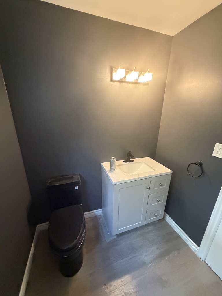 The finished bathroom — new white vanity, black toilet and vinyl plank flooring