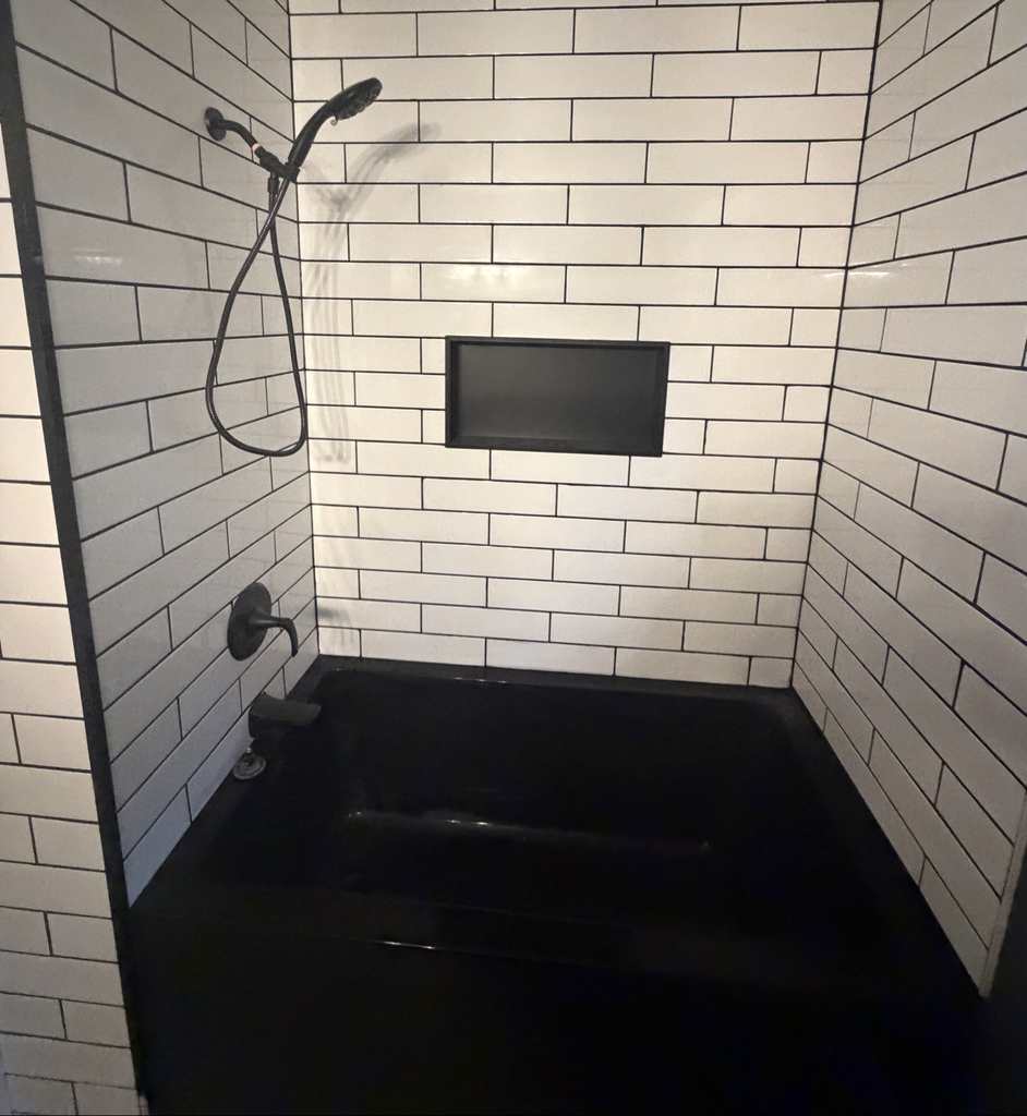 The rebuilt tub and shower — black tub, white subway tile with black grout and a black tiled niche